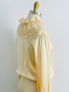 shoulder view of a mannequin display a vintage beige color satin blouse with lace ruffled collar