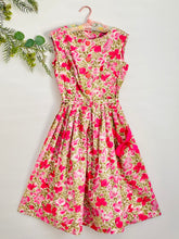 Load image into Gallery viewer, vintage 1950s pink floral dress with ribbon bow side pocket display on hanger
